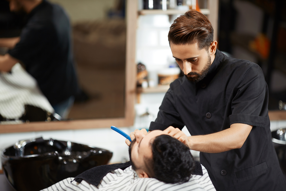 Young male hairstylist shaving beard